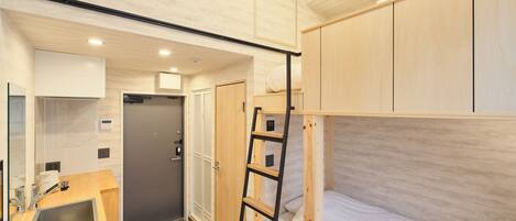 A compact room with a bunk bed, a small kitchenette, and a shower area.
