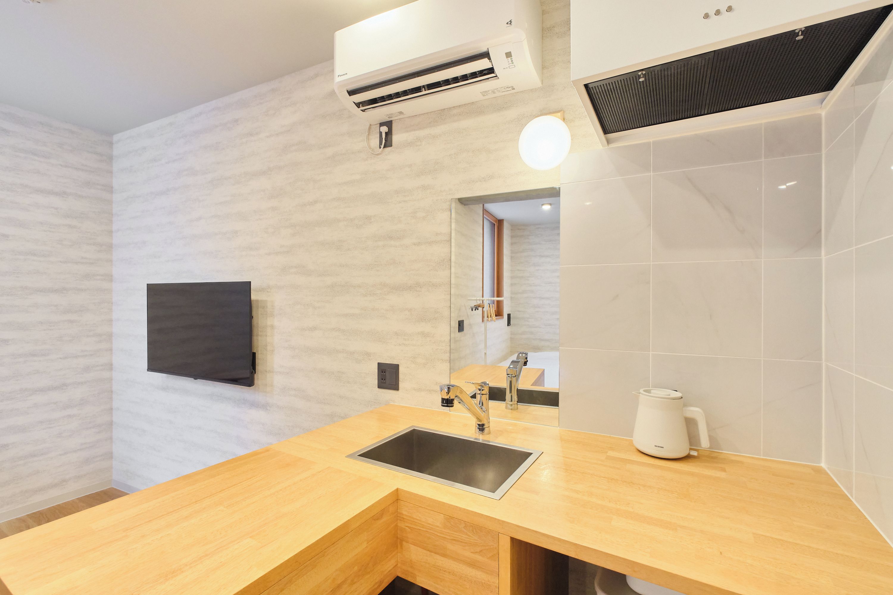 A modern bathroom with a wooden vanity, a sink, a mirror, a wall-mounted air conditioner, and a white kettle.