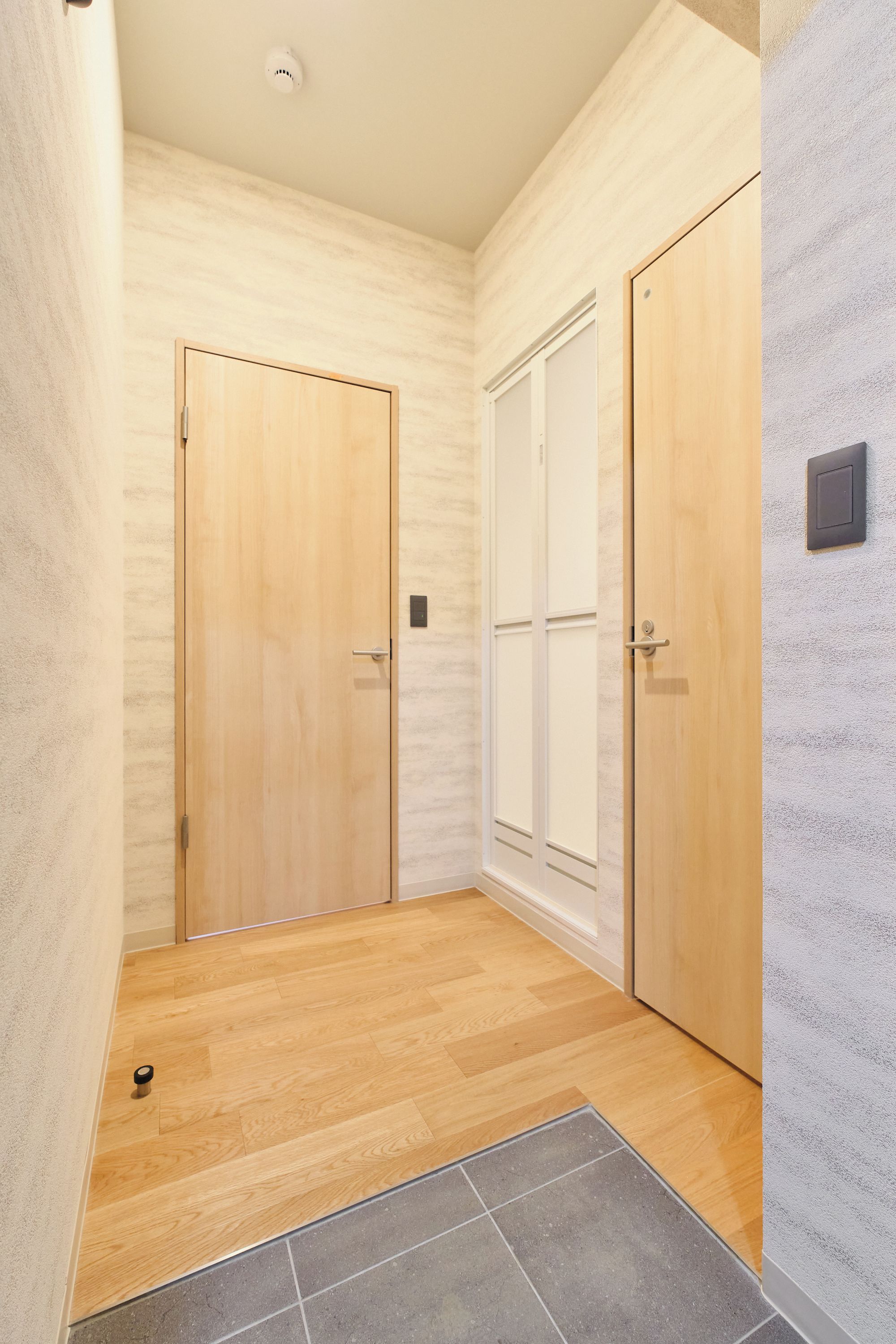 A hallway with two wooden doors, a textured wall, and a tiled floor.