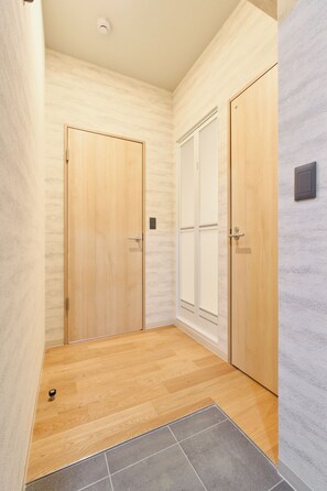 A hallway with two wooden doors, a textured wall, and a tiled floor. - Tomori (Tokyo)