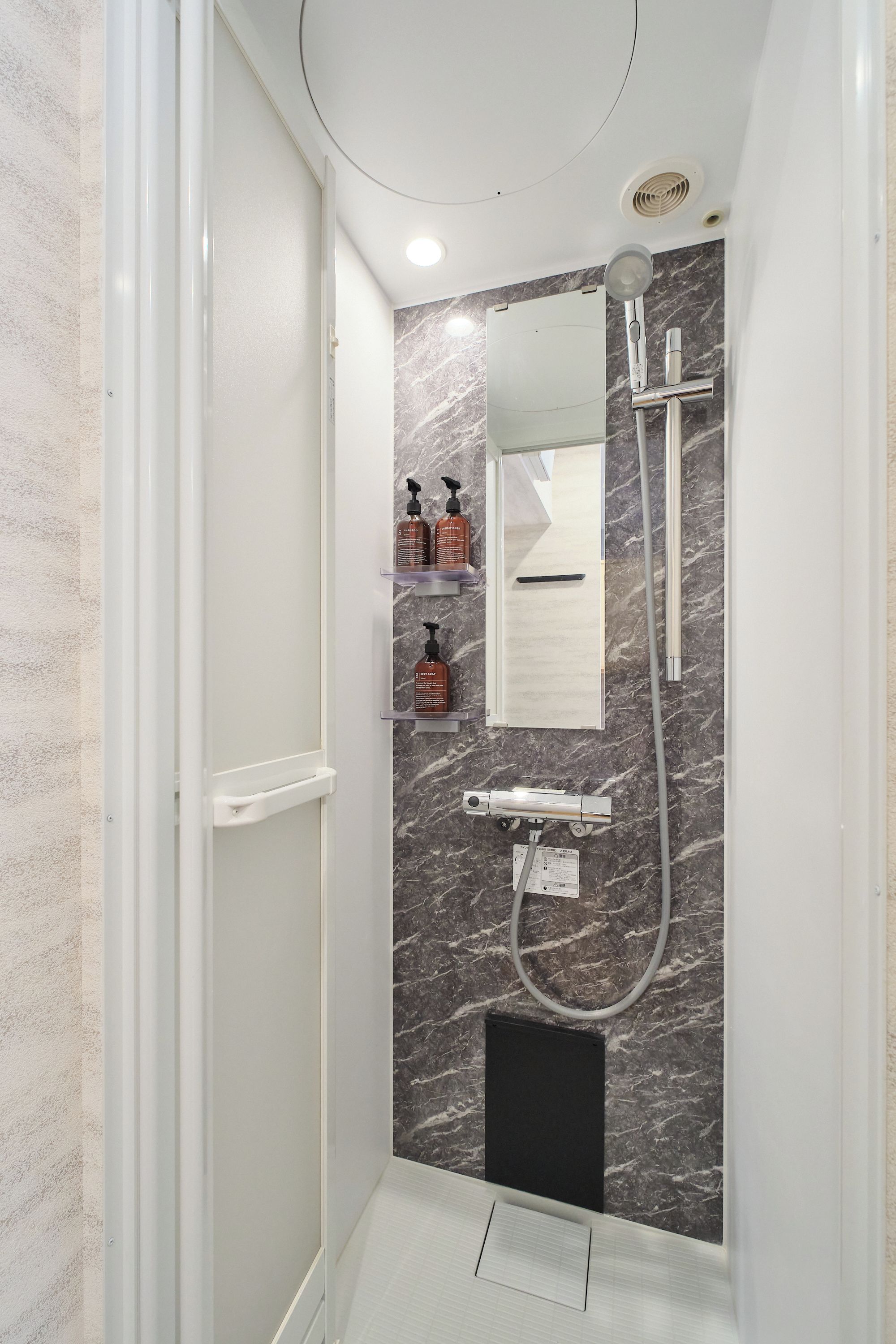 Ein modernes Badezimmer mit Dusche, Spiegel und Pflegeprodukten auf einem Regal.