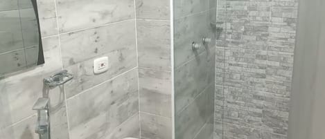 Een badkamer met een glazen wastafel, toilet en douche met een stenen muur.