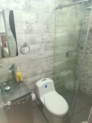 Ein Badezimmer mit Duschkabine aus Glas, Toilette und Waschbecken mit Seifenspender.