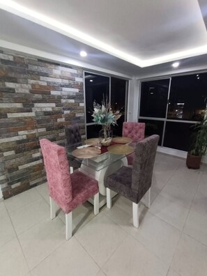 A dining area with a glass table and cushioned chairs, a decorative centerpiece, and a stone wall. - Hermoso apartamento amoblado en Meléndez City 403 (Cali)