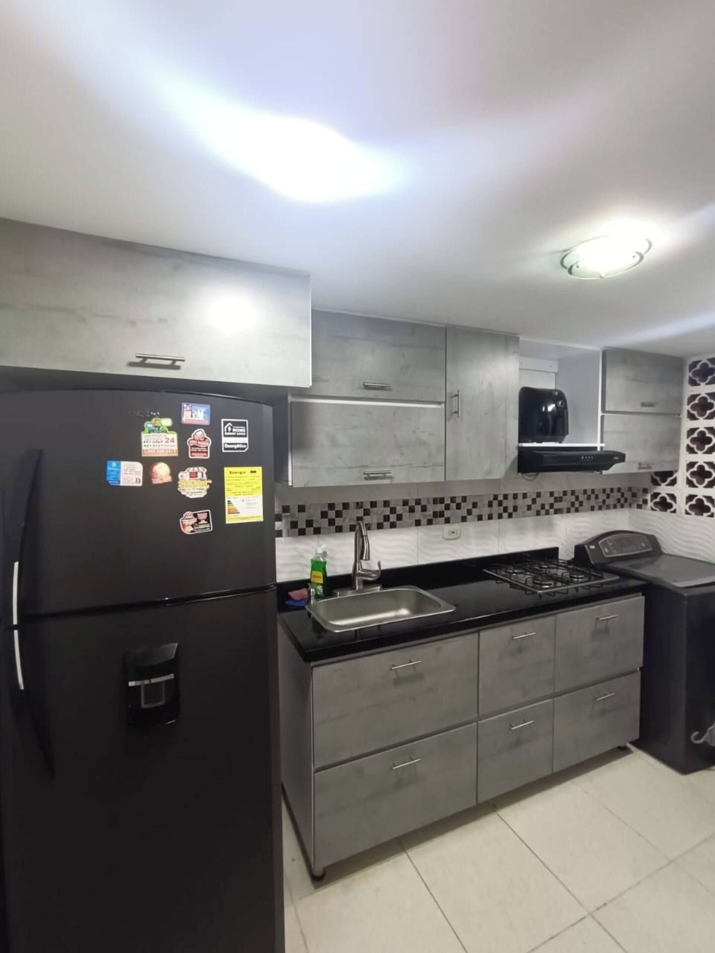 A modern kitchen with a refrigerator, stove, sink, and grey cabinets.
