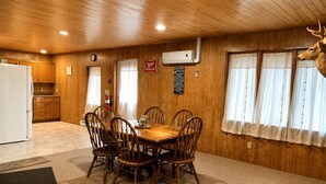 A wooden-paneled room with a dining table and chairs, a clock, an air conditioning unit, and a mounted deer head. - Rustic Cabin Escape in Welcoming Brown County. Reconnect, Relax & Unwind (Mount Sterling)