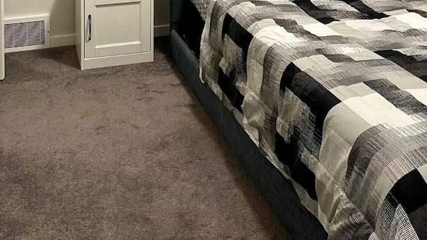 A bedroom with a bed, a nightstand, a lamp, and a painting on the wall. - Kennis Home (Airdrie)