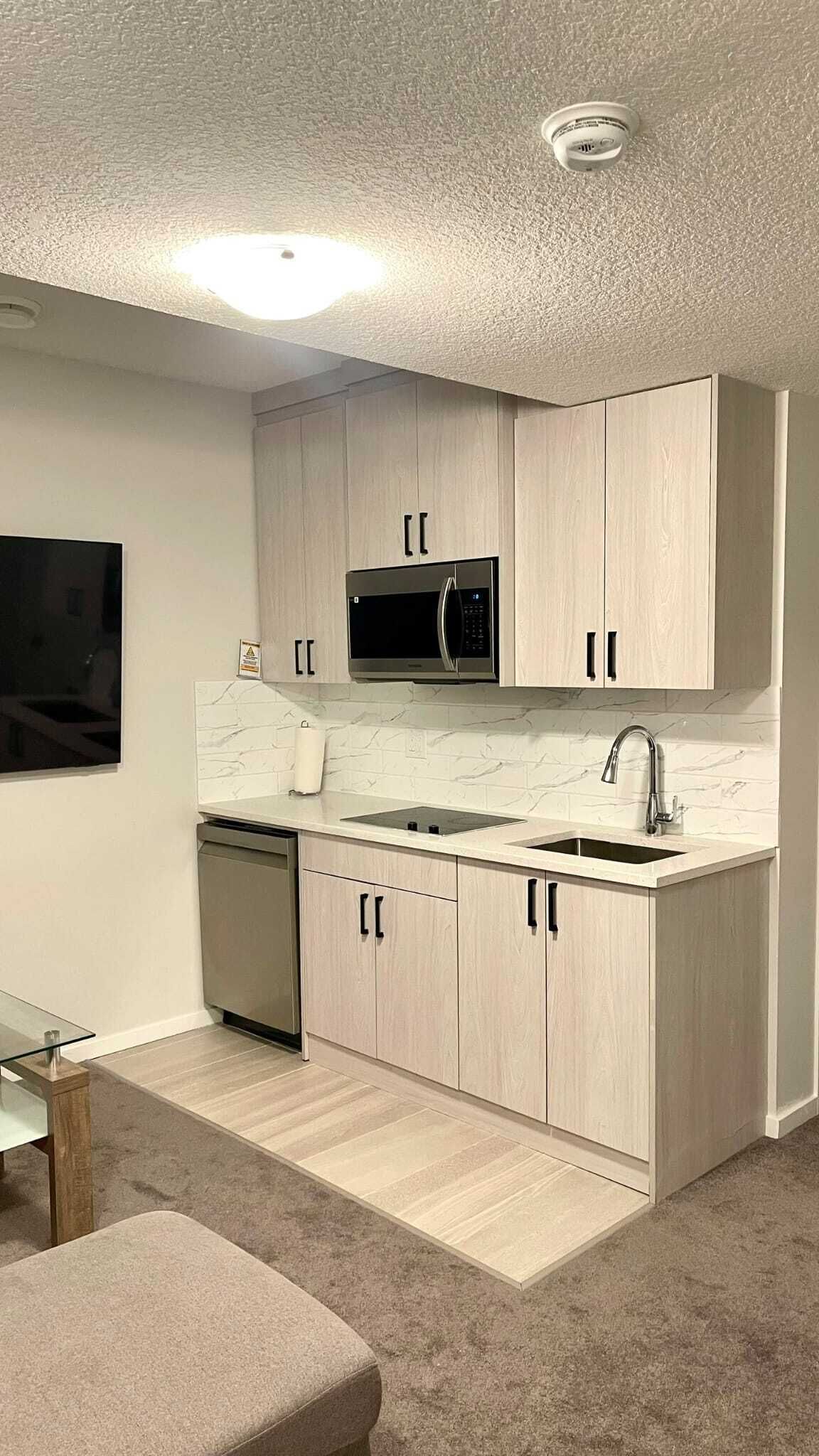 A compact kitchen with light wood cabinets, a microwave, a sink, and a dishwasher.