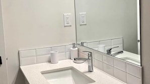 A modern bathroom with a large mirror, two sinks, and a toilet paper holder. - Kennis Home (Airdrie)