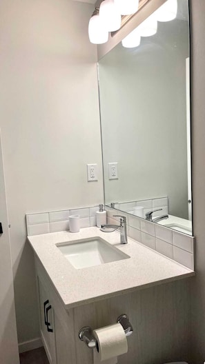 A modern bathroom with a large mirror, two sinks, and a toilet paper holder. - Kennis Home (Airdrie)