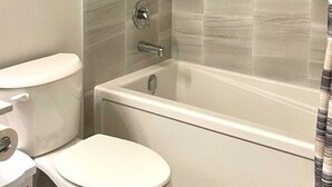 A bathroom with a toilet, a bathtub, and a shower area. - Kennis Home (Airdrie)