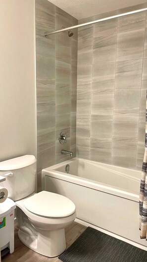 A bathroom with a toilet, a bathtub, and a shower area. - Kennis Home (Airdrie)