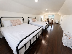 Een kamer met twee bedden, een houten vloer, een raam en een klein tafeltje met stoelen.