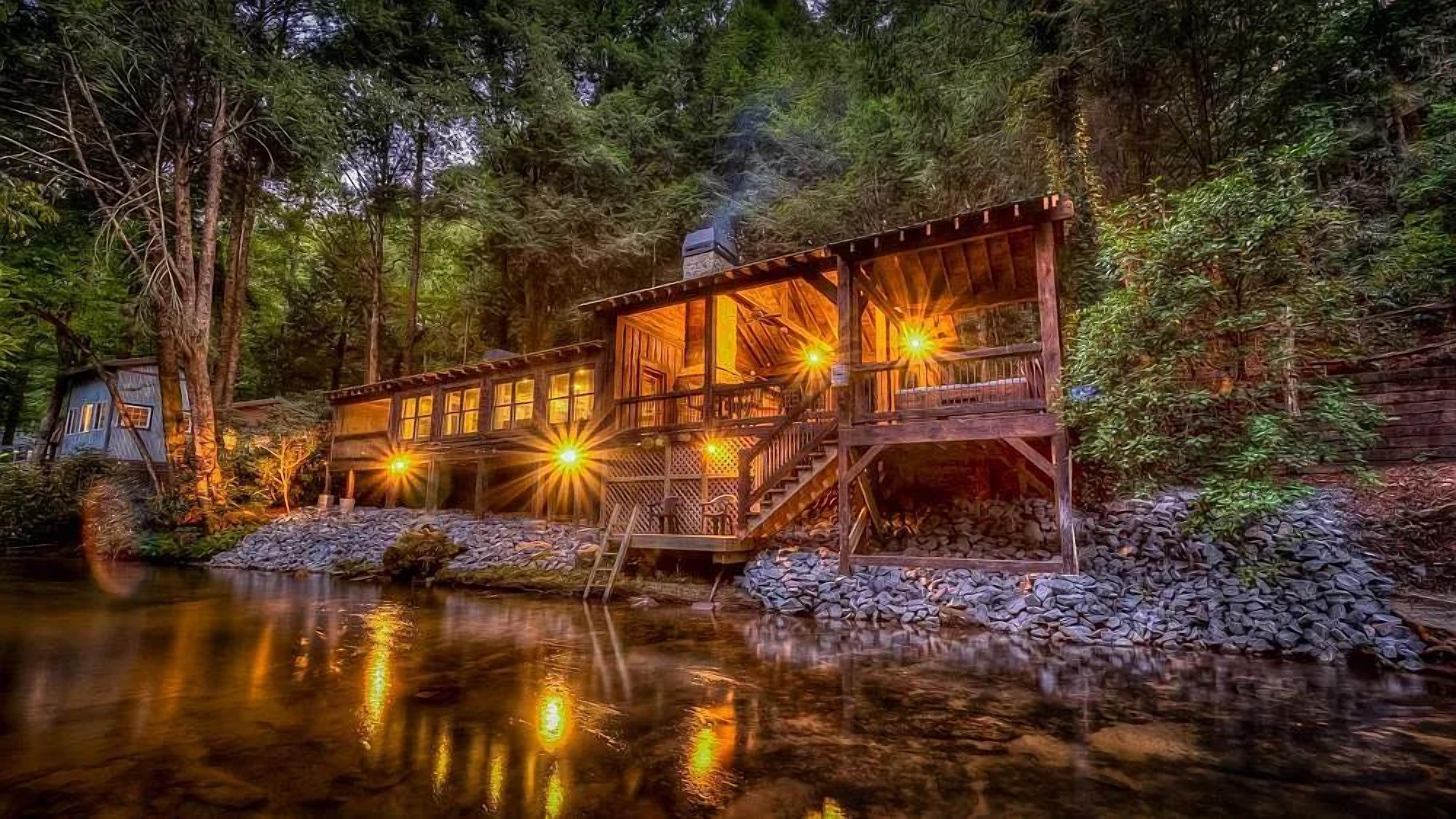 A wooden cabin with a deck and a stone pathway leading to a reflective water body.
