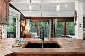 Una cocina rústica con un lavamanos grande, encimeras de madera y vistas al exterior a través de amplios ventanales.