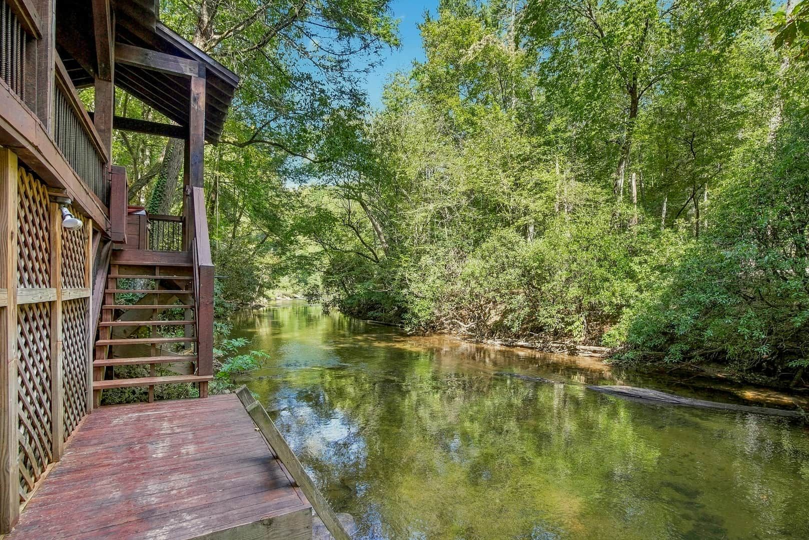 A wooden deck leading to a river with dense greenery on both sides.