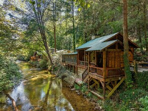 Een houten chalet met een terras dat uitkijkt over een rivier, omgeven door dicht bos.