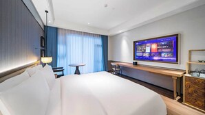 Habitación de hotel con una cama grande, un escritorio, un televisor y vistas a la ciudad.