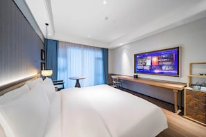 A hotel room with a large bed, a desk, a television, and a view of the city. - Manxin Mansion (Jingzhou)