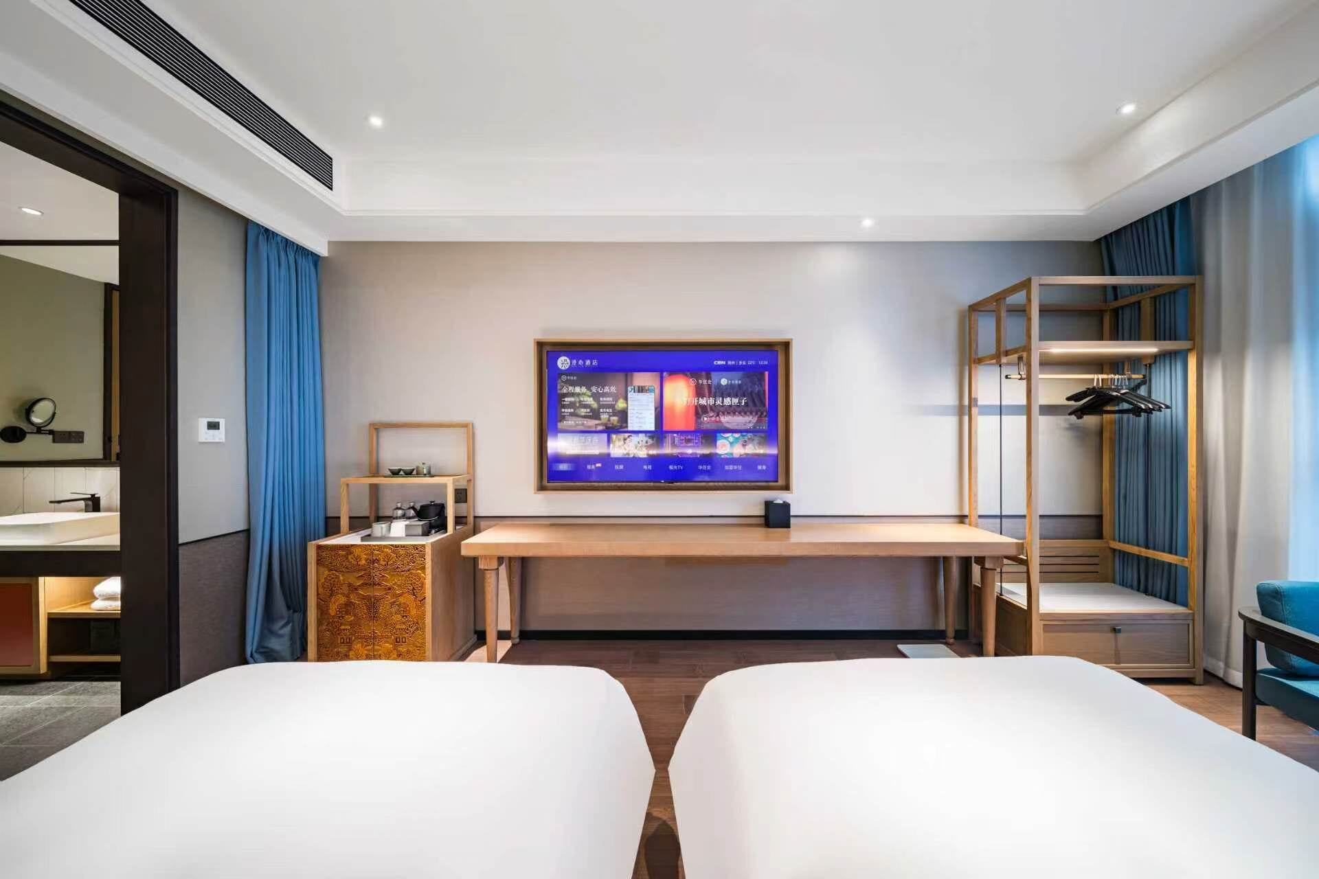Habitación de hotel con cama, escritorio, televisor, armario y baño visible a través de una puerta abierta.