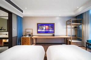 Habitación de hotel con cama, escritorio, televisor, armario y baño visible a través de una puerta abierta.