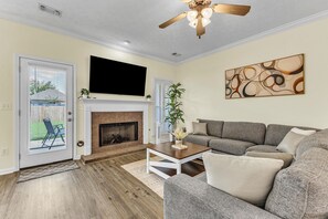 Ein Wohnzimmer mit Kamin, großem Flachbildfernseher, Deckenventilator und grauem Sofa.