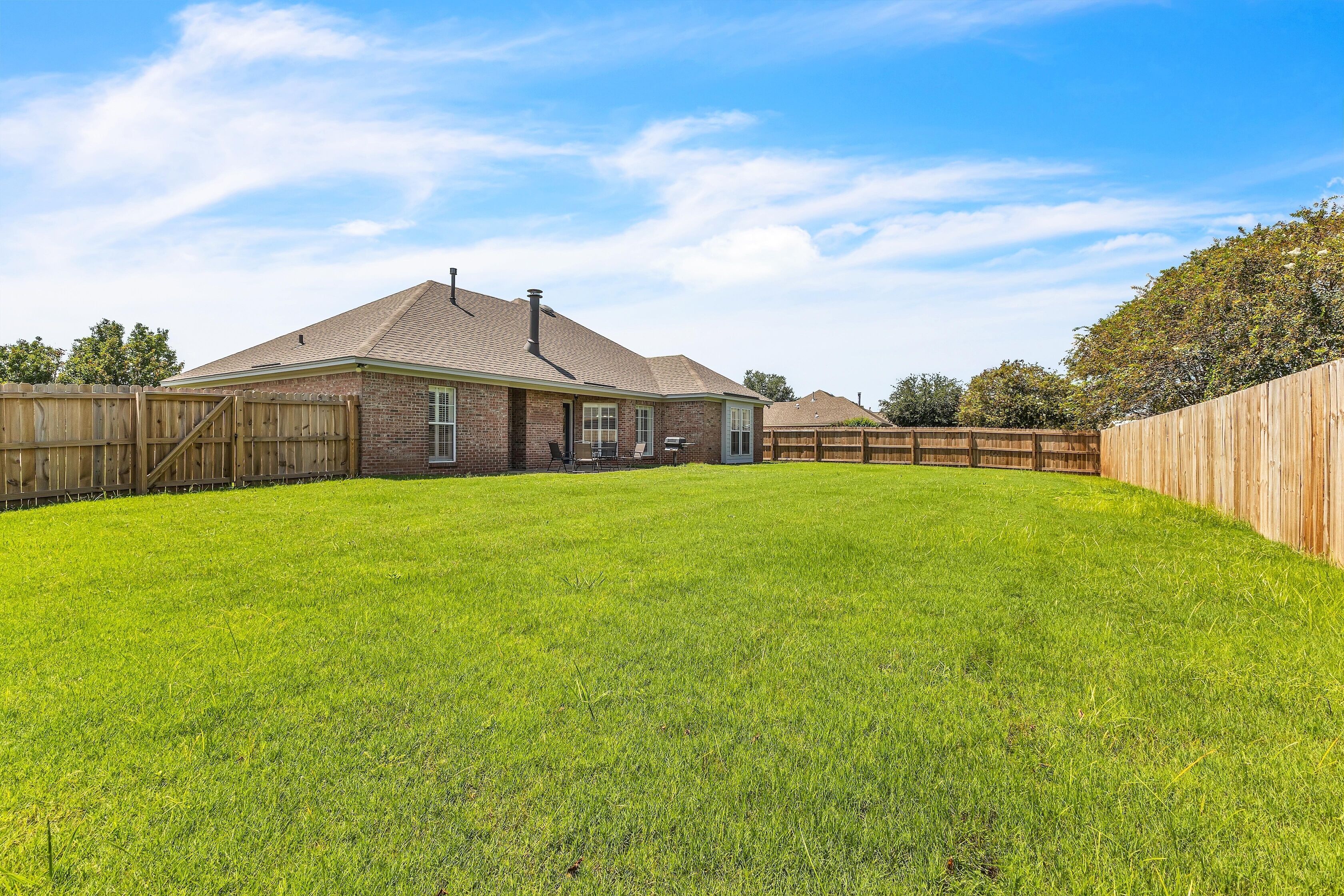A residential backyard with a brick house, a wooden fence, and a well-maintained lawn.