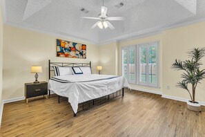 Ein Schlafzimmer mit einem Bett, Nachttischen, einem Deckenventilator, einem Fenster mit Jalousien und einer Pflanze.