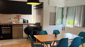 Una cucina moderna con zona pranzo, pavimento in legno e un'ampia finestra con persiane.