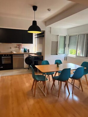 Cozinha moderna com área de jantar, piso de madeira e uma grande janela com persianas.