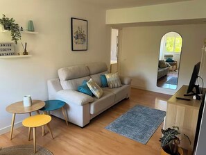 Sala de estar com sofá, duas mesinhas, tapete, espelho e escrivaninha com computador.