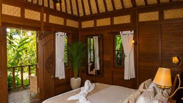 A room with a bed, a ceiling fan, a potted plant, and a view of greenery outside.