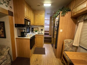 A compact RV kitchen with wooden cabinets, a microwave, a refrigerator, and a small dining area.