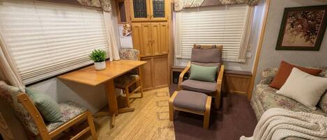 A compact RV interior with a wooden table, two chairs, a sofa, and a small plant.