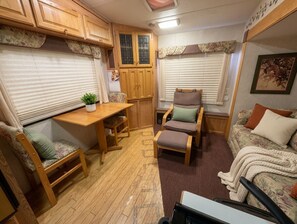Interior compacto de una caravana con una mesa de madera, dos sillas, un sofá y una planta pequeña.
