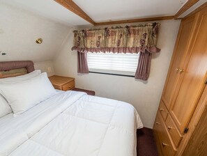 A bedroom with a bed, a wooden wardrobe, a window with curtains, and a wall-mounted light fixture.
