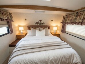 Quarto com cama, duas mesas de cabeceira, luminárias, janela com cortinas e cabeceira com desenho floral.