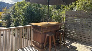 Una terraza exterior de madera con zona de barbacoa, una mesa y un banco.