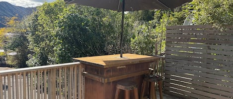 Una terraza exterior de madera con zona de barbacoa, una mesa y un banco.