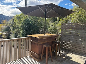 Una terraza exterior de madera con zona de barbacoa, una mesa y un banco.