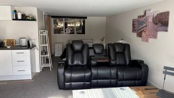 A modern living room with a black leather sofa, a white coffee table, and a kitchen area with a kettle and coffee maker.