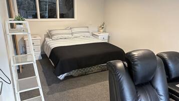 A bedroom with a bed, a nightstand, a dresser, a chair, and a window.