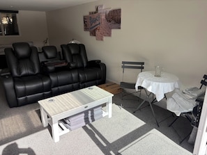 A living room with a black leather sofa, a white coffee table, a small table with a pitcher, and a wall-mounted artwork. - Perfect Marlborough Sounds cabin retreat for your Sandy Bay getaway (Black Rock)
