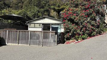A small, single-story building with a flat roof, a wooden fence, and a gravel driveway.
