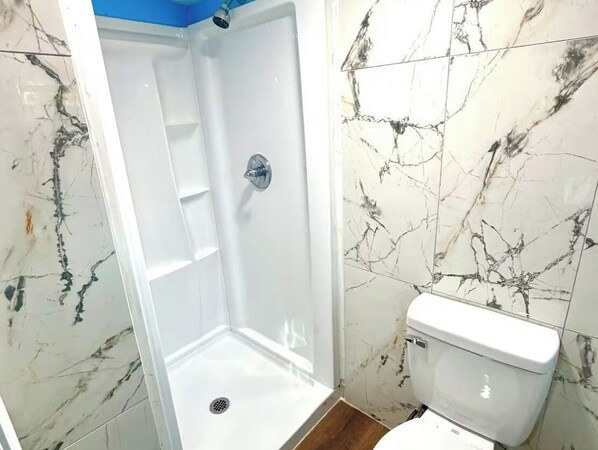 A bathroom with a shower, toilet, and marble-patterned walls. - Tiny Rock Retreat - Big Style - 5 Mins From DT (Jacksonville)