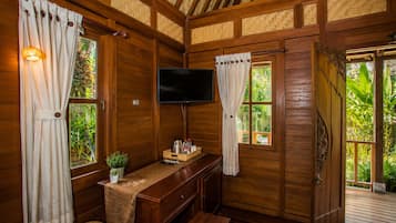 Una habitación con piso de madera, un televisor, un escritorio y una ventana con cortinas.