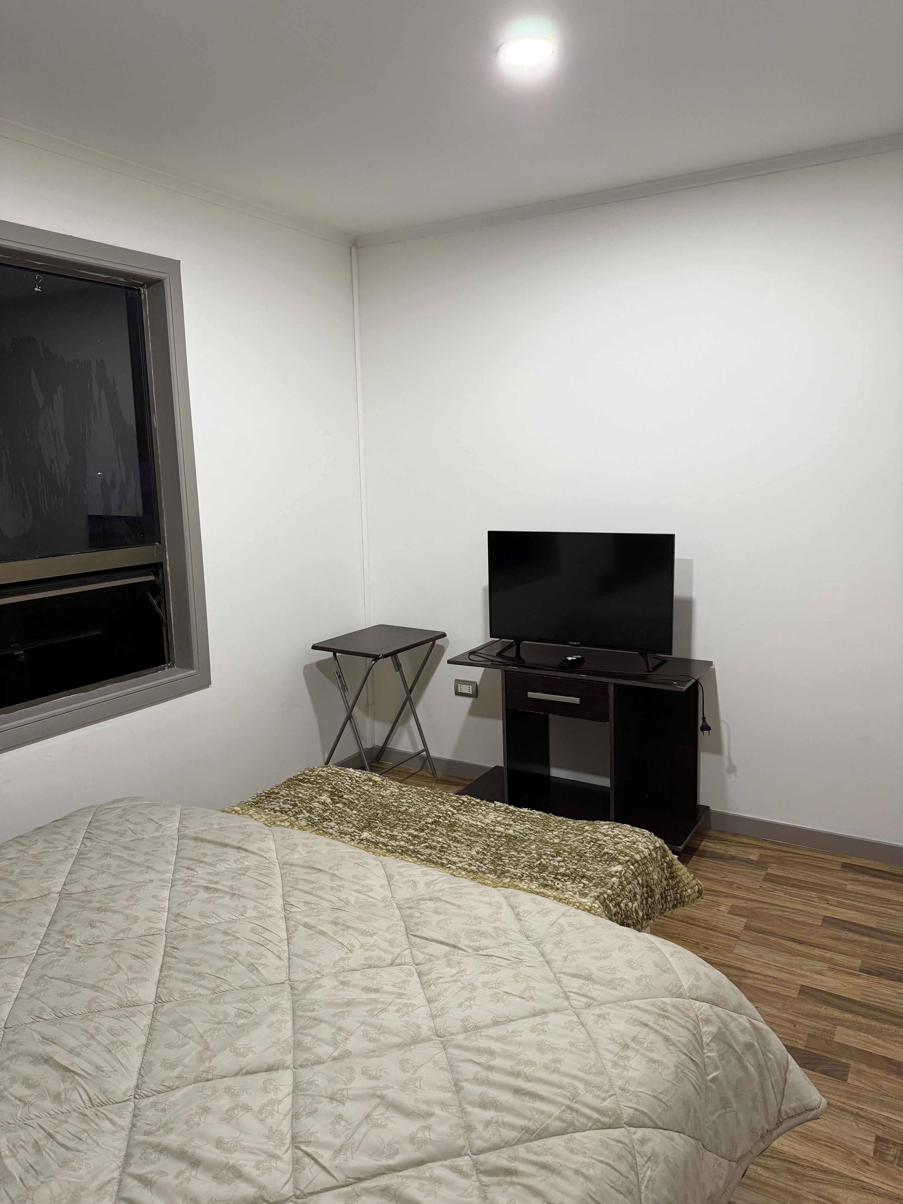 Une chambre à coucher avec un lit, un bureau, une télévision et une fenêtre.