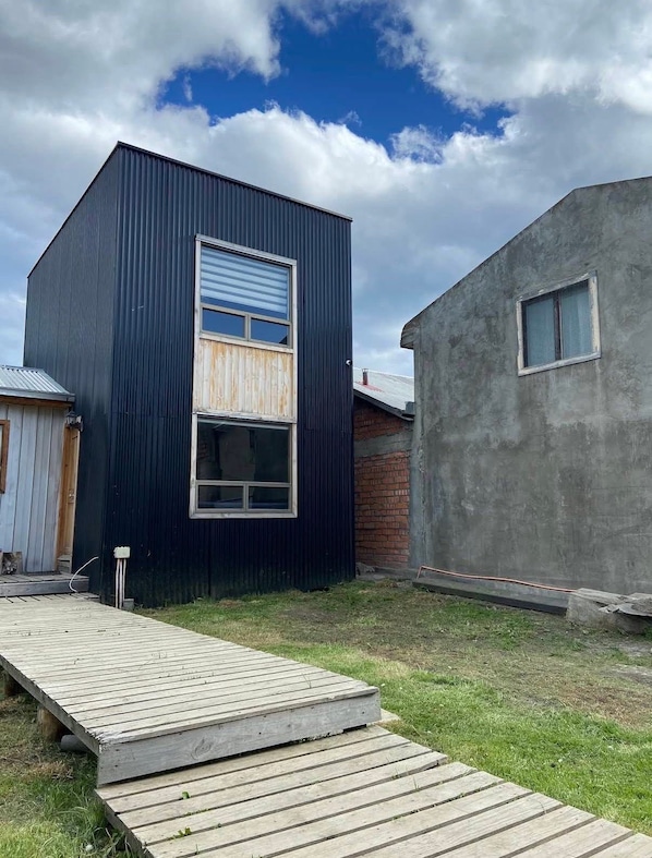 A modern building with a dark exterior, a wooden deck, and a small adjacent structure.
