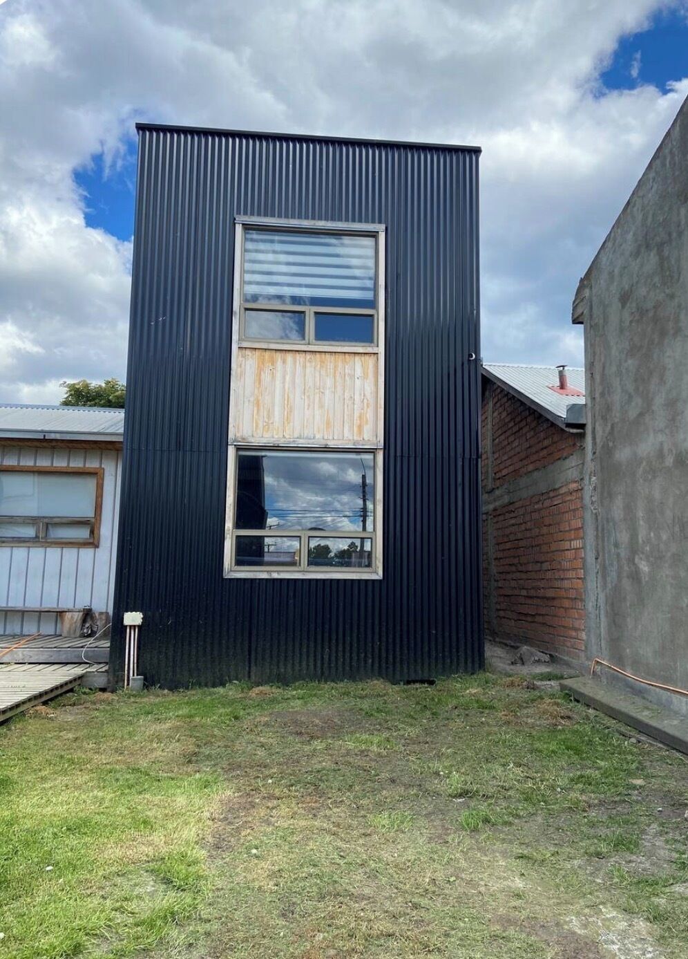 Un bâtiment moderne avec une façade en métal ondulé, une grande fenêtre et une cour verdoyante.