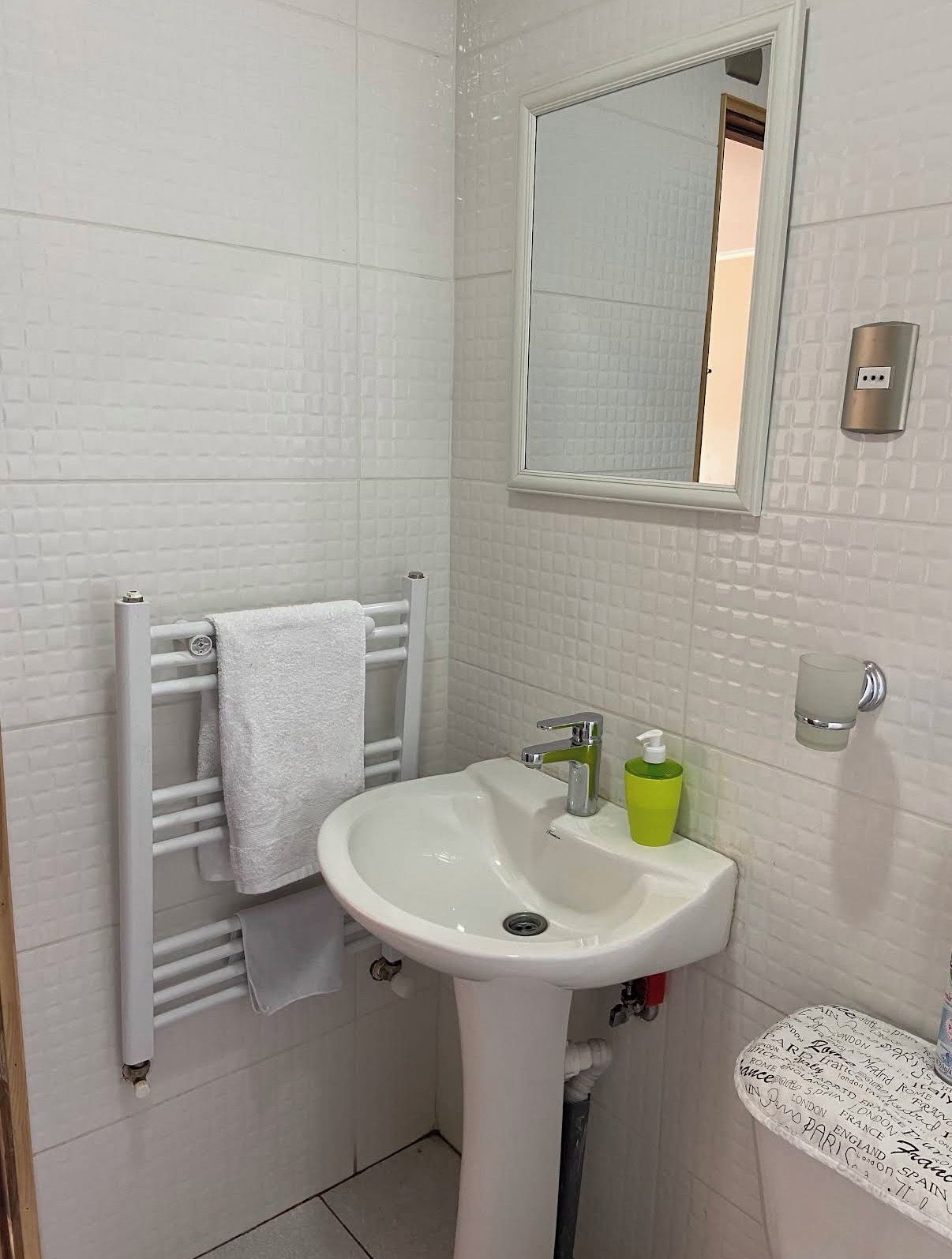 A bathroom with a white sink, a towel rack, a mirror, and a glass soap dispenser.